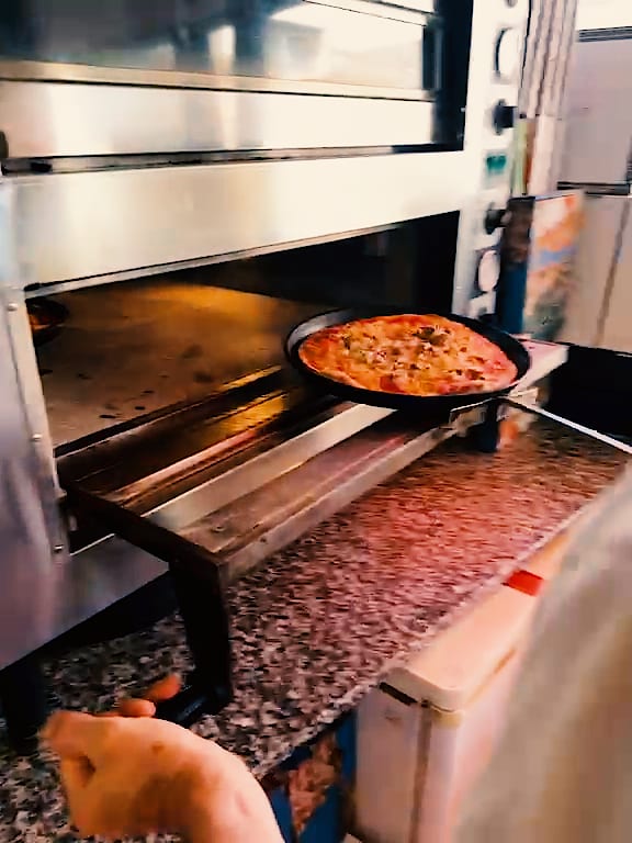 Eine fertig belegte Pizza wird in den Ofen geschoben